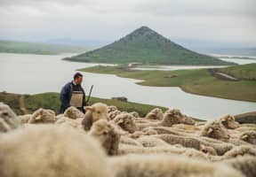 Ganadero con las cabras en una esplanada con un precioso lago de fondo